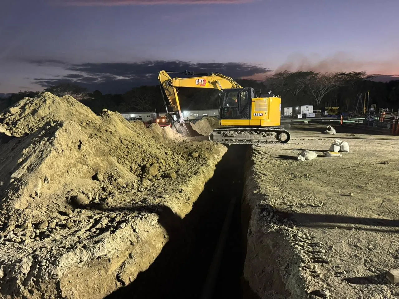 Excavadora maniobrando en zanja de tubería al atardecer